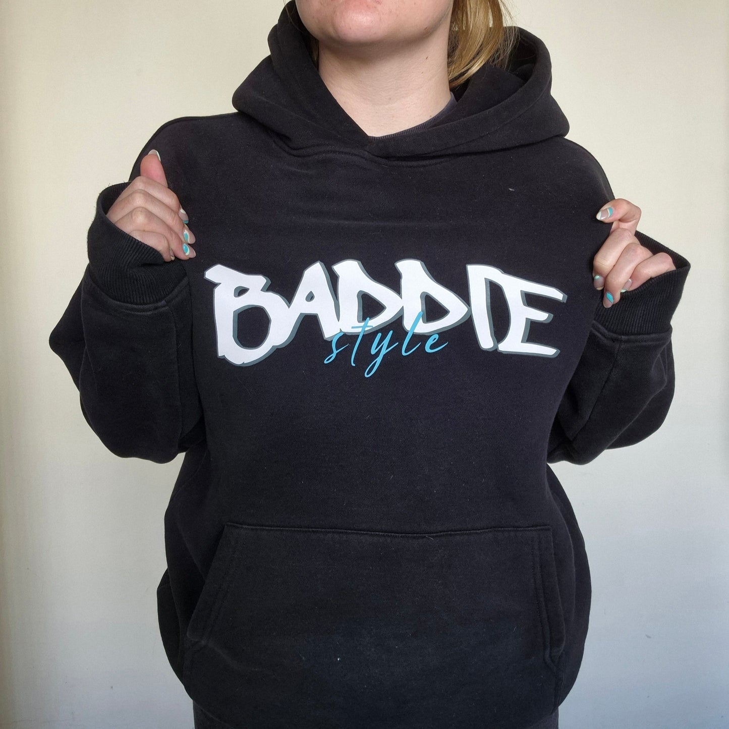 Person wearing a black hoodie with 'BADDIE STYLE' text on a plain background
