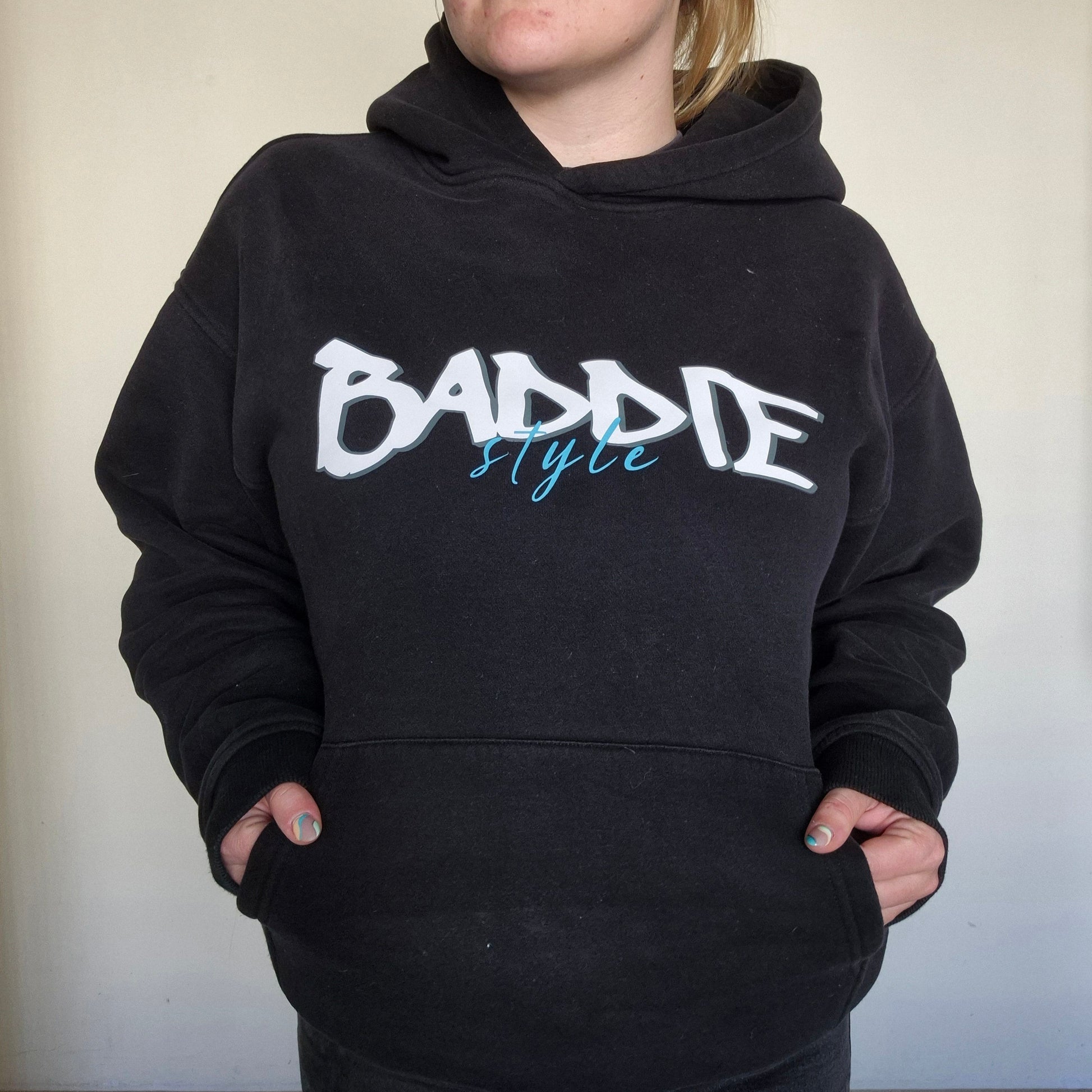 Person wearing a black hoodie with 'Baddie Style' text on a plain background
