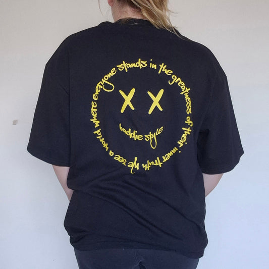 Person wearing a black t-shirt with yellow text and symbols on the back, standing against a plain white wall.