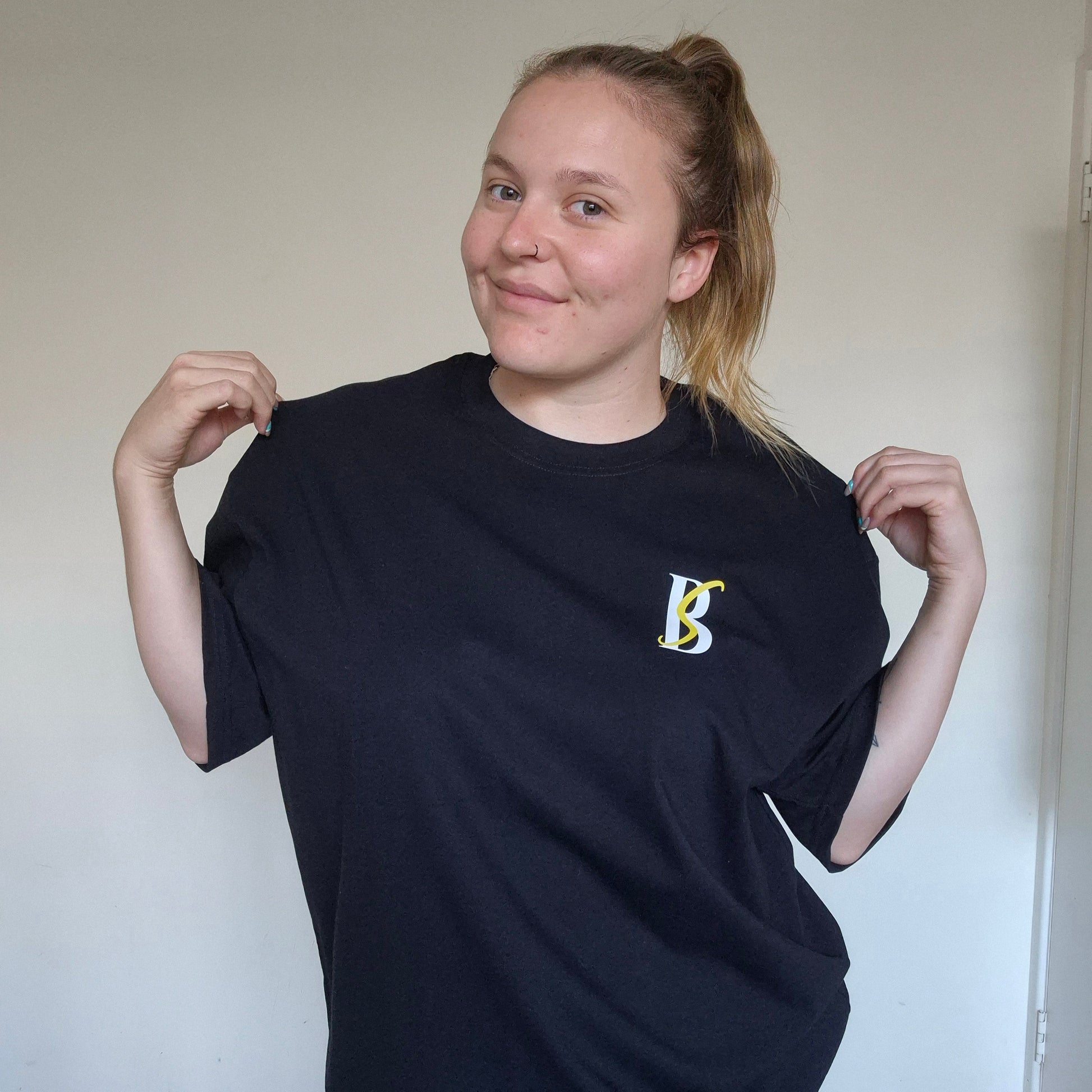 Person wearing a black t-shirt with a logo, standing against a plain background
