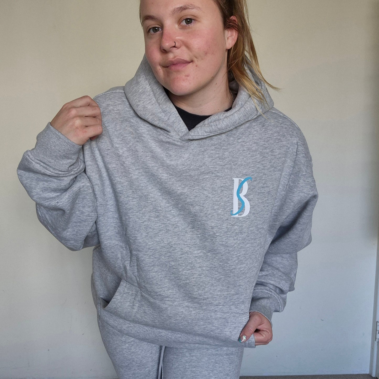 Person wearing a gray hoodie with a logo, standing against a plain background