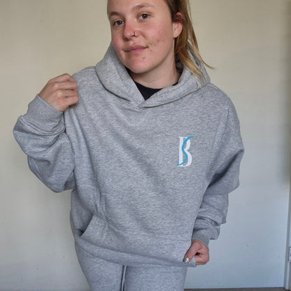 Person wearing a gray hoodie with a logo, standing against a plain background