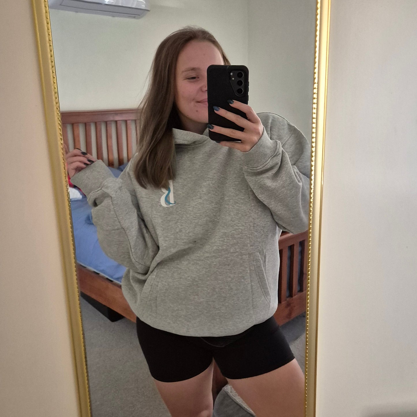 Person taking a mirror selfie wearing a gray sweatshirt and black shorts in a room.