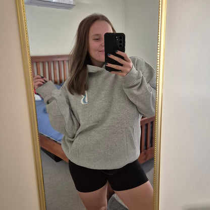 Person taking a mirror selfie wearing a gray sweatshirt and black shorts in a room.