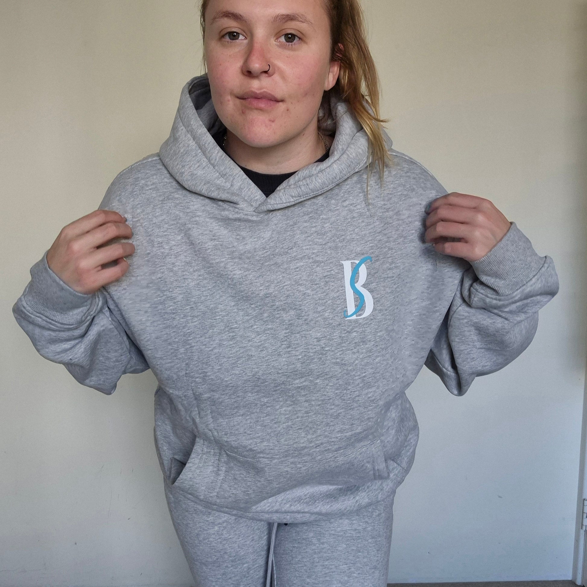 Person wearing a gray hoodie with a logo, standing against a plain background